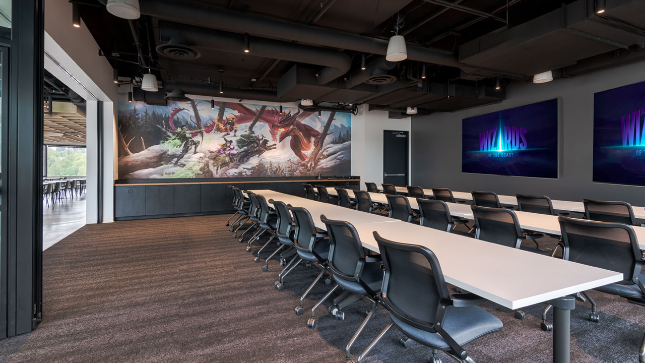 Sala de reuniões da Wizards of the Coast em Renton, com mesas, cadeiras e mural de fantasia.